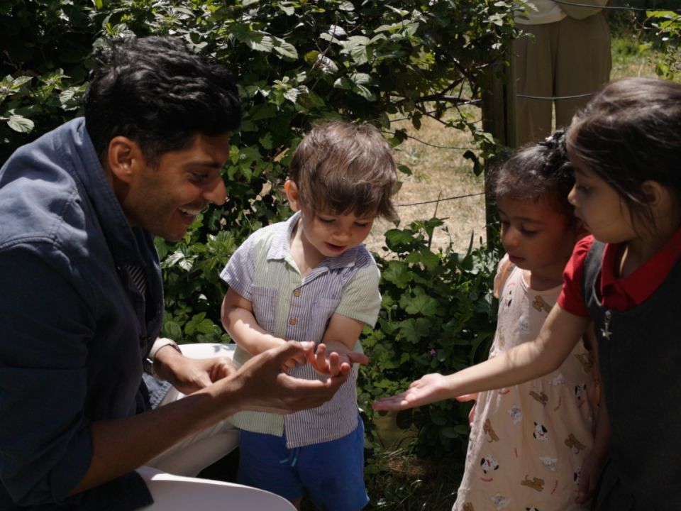 A man and three kids looking at creepy crawlies in an orchard